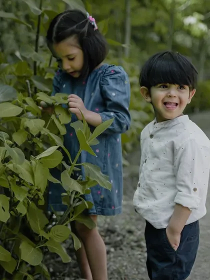 Siblings exploring the leaves on a bush, a great example of a candid moment captured during an outdoor adventure.