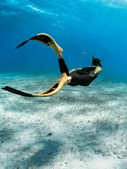 A freediver glides effortlessly through clear water using the Aqualung Cyclone X long blade fins. These fins are designed for maximum power transfer and efficiency, allowing for deeper dives with less effort, perfect for the art of freediving.