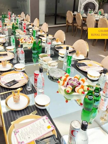 A royal dining setup featuring a long, reflective table adorned with gold-rimmed plates and cutlery. This arrangement is perfect for a formal sit-down dinner, providing a sense of grandeur and exclusivity for your guests.