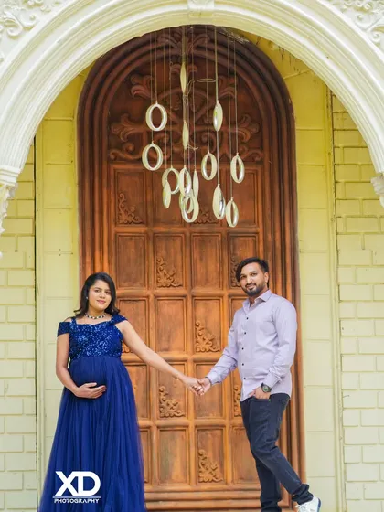 A classic couple's portrait, holding hands in front of an elegant, grand wooden door.
