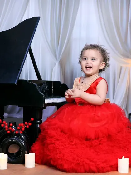 A joyful little girl in a red dress, laughing as she plays by the miniature piano.