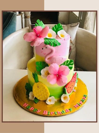 A vibrant tropical flamingo cake with two tiers, decorated with hibiscus flowers, pineapples, and watermelon slices for a summer birthday.