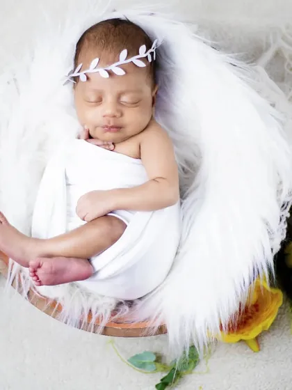 A swaddled baby boy wearing a leaf crown, sleeping peacefully in a bowl with white fur.