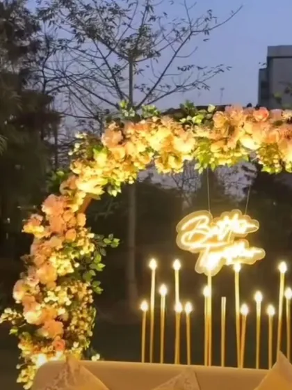 An outdoor photo corner for an engagement party, featuring a semi-circular floral arch, candle-like LED lights, and a "Better Together" neon sign.