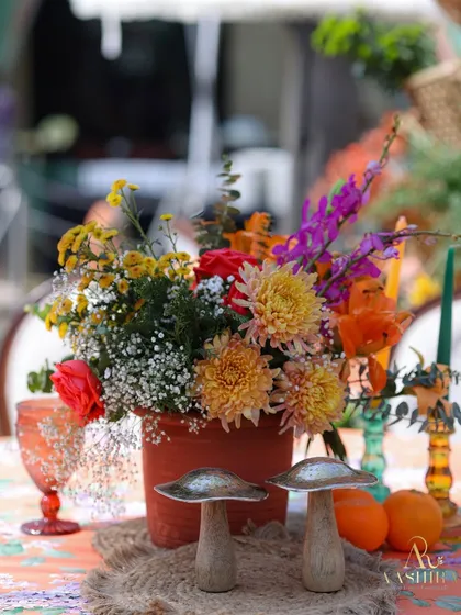 A rustic and whimsical centerpiece with a terracotta pot of wildflowers, quirky wooden mushroom accents, and colored glassware.