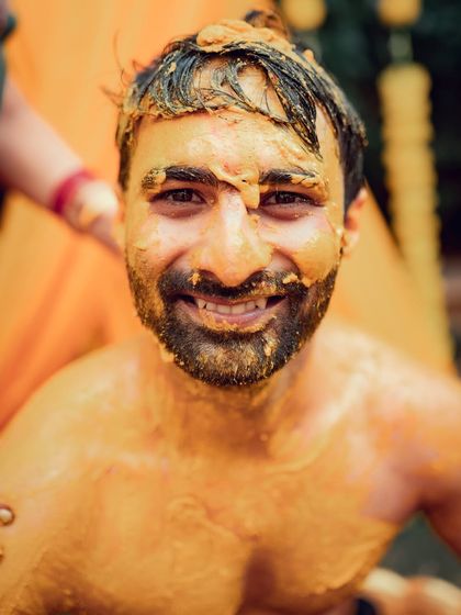 A close-up of the groom's face covered in turmeric paste, capturing his joyful and uninhibited reaction during the Haldi rituals.