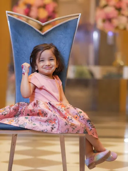 A charming portrait of a little girl in a lovely pink floral dress. I use elegant props like this chair to add a touch of sophistication to children's photoshoots.