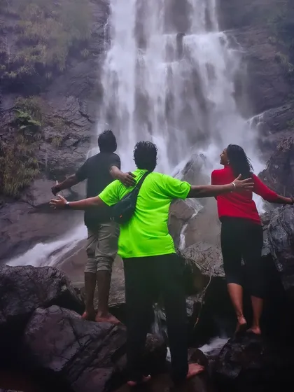 A creative shot of three friends with arms outstretched before a waterfall, embracing the moment.