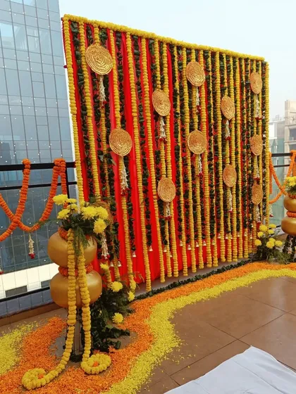 Even a modern space like a terrace can be transformed for a traditional ceremony. For this Haldi function, I created a vibrant backdrop using vertical strings of yellow and orange marigolds against a red fabric panel, accented with traditional woven discs.