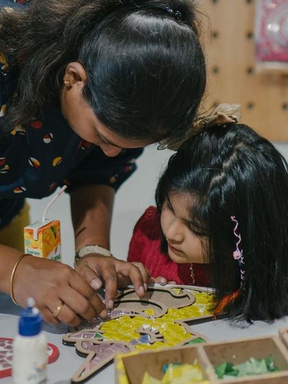 A close-up shot of a mother guiding her daughter through a mosaic art project during a birthday party. These shared moments of focused creativity are what make an art party so special.