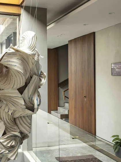 The intricate folds of the 'Radha Krishna Raas Leela' installation seen from a glass bridge. This perspective highlights the texture and form of the piece, which serves as a central artistic feature connecting different levels of the home.