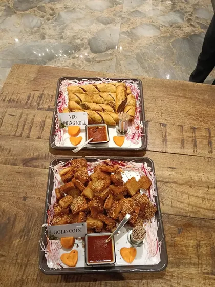 A platter of classic crowd-pleasers. We serve crispy Veg Spring Rolls and savory Gold Coin appetizers, both fried to golden perfection and accompanied by a sweet and spicy dipping sauce.