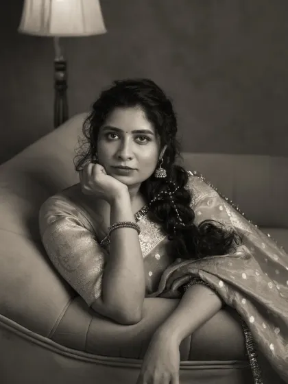 A thoughtful monochrome portrait of Vennela, resting her chin on her hand. The vintage furniture and her traditional attire create a nostalgic scene, and the black and white rendering adds to the feeling of a memory captured in time.