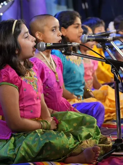 A side view of our young students singing in unison during their devotional music segment. Each student has their own microphone, learning proper mic technique from an early age.