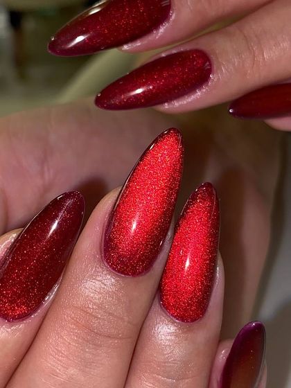 A dramatic, stiletto-shaped manicure featuring a vibrant red cat-eye effect. The sharp shape and mesmerizing polish create a bold and powerful look.