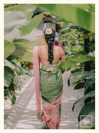A beautiful shot of the bride from behind, showcasing her intricate hairstyle adorned with flowers and the elegant drape of her green and pink saree.