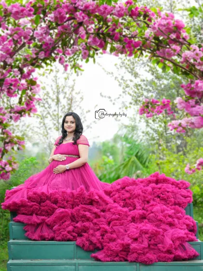 A magnificent shot featuring a vibrant pink ruffled gown spread out on green steps, framed by a beautiful pink floral arch.