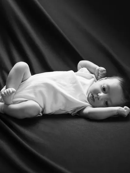 A full body shot in black and white shows this newborn stretching out on a dark, soft fabric. The contrast creates a dramatic and timeless portrait.