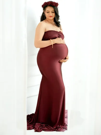 A sweet and romantic portrait. The mom-to-be wears a floral crown that complements her maroon gown, adding a touch of softness and femininity.