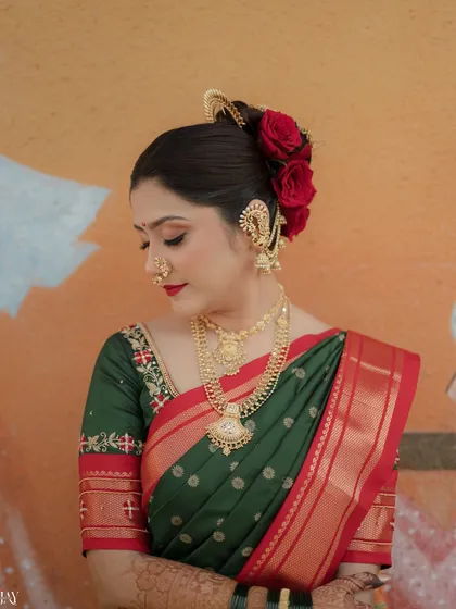 A detailed close-up of the bride's profile, showcasing her traditional Maharashtrian bridal look. The focus is on the intricate hairstyle with red roses, the classic nath, and layered gold jewelry.
