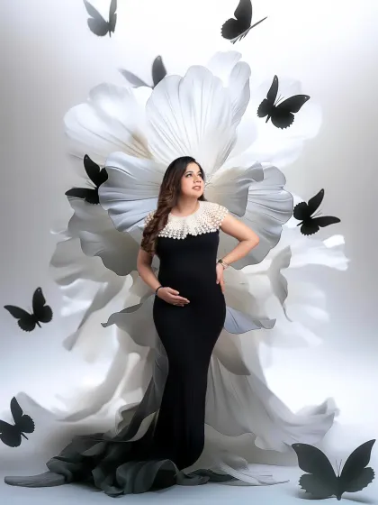 A beautiful and creative composition. The mother-to-be in a black gown is framed by a large white flower and fluttering black butterflies, creating a striking visual narrative.