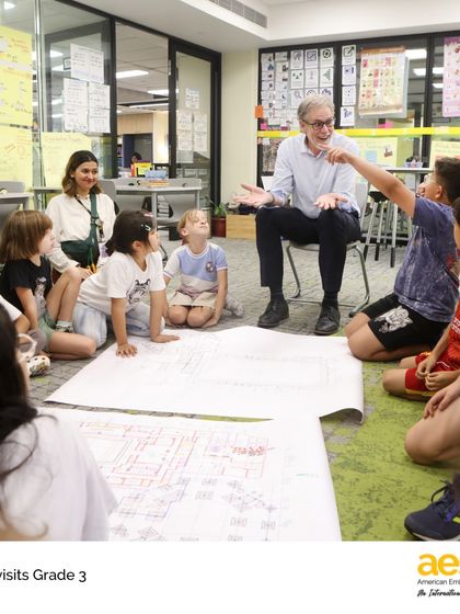 Our school director sits with third-grade students to review the master plans for a new gymnasium. This visit was in response to their persuasive letters advocating for more recess, showing them their voices matter.