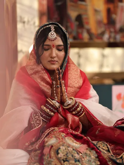 A serene moment captured for a traditional Marwadi bride. The makeup is subtle yet defined, with a focus on flawless skin, a classic red bindi, and defined eyes to complement the royal bridal attire and intricate jewelry.