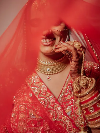 A playful close-up of the bride peeking through her red veil. This shot is full of joy and coyness, capturing a classic bridal moment.