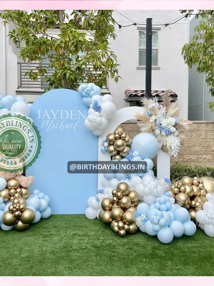 An elegant outdoor setup with a sky-blue backdrop and a balloon arrangement in blue, white, and gold. The pampas grass and floral arrangement add a touch of boho chic.
