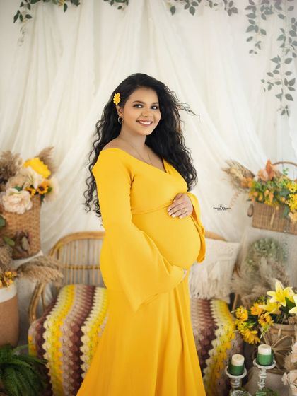 A classic and beautiful solo portrait. The mother-to-be looks directly at the camera with a warm smile, glowing in her yellow dress.