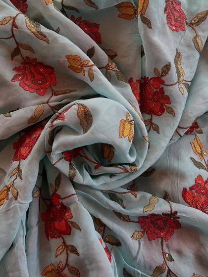 A beautiful sky blue organza with vibrant red and yellow floral embroidery. This fabric is a perfect example of how organza can carry bold designs while remaining light and airy.