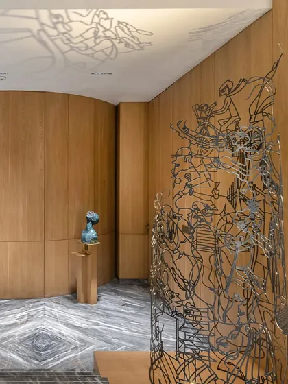 This illuminated mild steel installation, titled 'Moving Cache', stands as a delicate sculpture on a staircase landing. Its intricate form casts ephemeral shadows on the ceiling, depicting scenes from a family's shared journeys.
