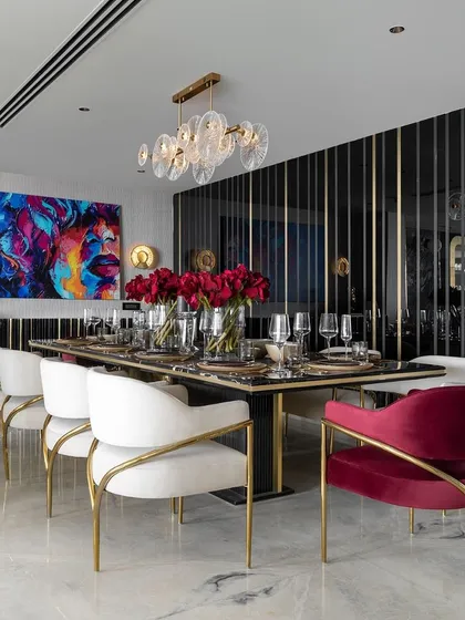 A bold and dramatic dining room setting. We used chairs in contrasting white and red velvet with v-shaped gold frames to create a high-impact look, complemented by a large piece of abstract art.