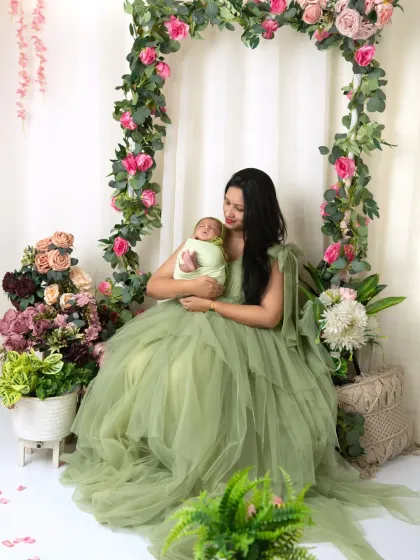 A full-length portrait of a mother in an elegant green gown, holding her newborn in our floral studio.