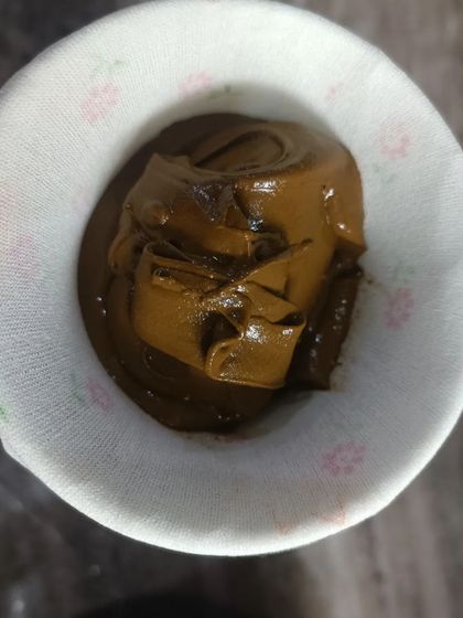 Straining the henna paste through a cloth. This step is essential to remove any small lumps and create an ultra-smooth paste that flows easily from the cone.