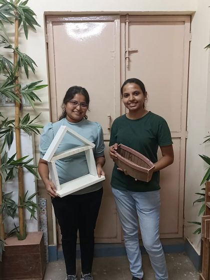 Bhoomika and Samrakshini with their finished projects. One made a house-shaped shelf, and the other created the kerf-bent boat planter.