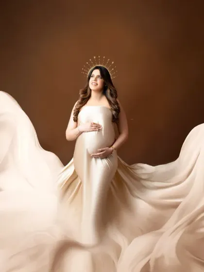 A divine moment captured in our studio. The mother-to-be wears a satin gown with a halo effect, surrounded by billowing fabric that creates an ethereal, angelic look.