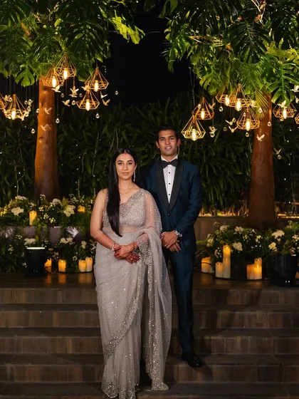 The couple's portrait at their reception, with trees adorned with geometric lanterns and candles creating a romantic backdrop.