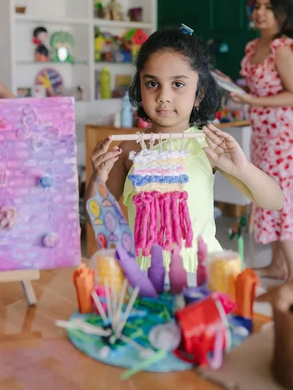 This young artist is proudly displaying her creations from our summer art camp, including a vibrant woven wall hanging. Each piece reflects her unique creativity and the new skills she learned.