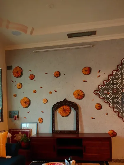 A wide view of a traditional kolam mural I painted in a client's living room. The design, reminiscent of patterns drawn on a grandmother's floor, brings a sense of heritage and celebration into a modern home. The scattered marigold flowers add a feeling of warmth and festivity to the space.