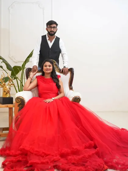 Posing like royalty for your pre-wedding shoot. The bride-to-be is radiant in a voluminous red ball gown, seated elegantly beside her partner.