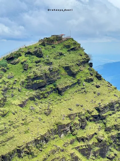 A close-up shot of the Deviramma Betta peak, highlighting its rugged texture and the small shrine at its summit.