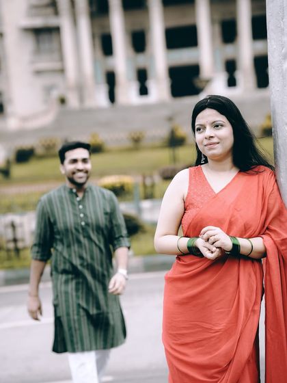 A creative composition with the bride in focus and the groom approaching in the background, set against the Vidhana Soudha.
