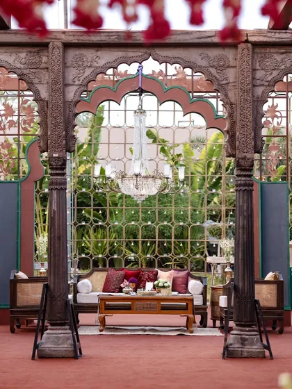 A regal seating area framed by intricately carved wooden pillars and arches. The crystal chandelier adds a touch of classic elegance to the traditional Indian architectural elements.