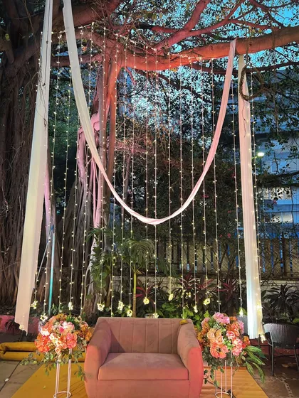 A romantic and dreamy photo booth created by hanging curtains of fairy lights from a large tree. The simple armchair and floral arrangements provide the perfect spot for beautiful portraits.