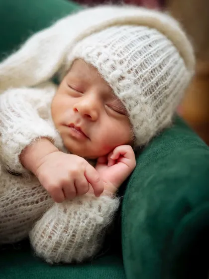 A detailed close-up of a newborn's face, sleeping peacefully in a soft, white knit hat. I love capturing these tiny features.