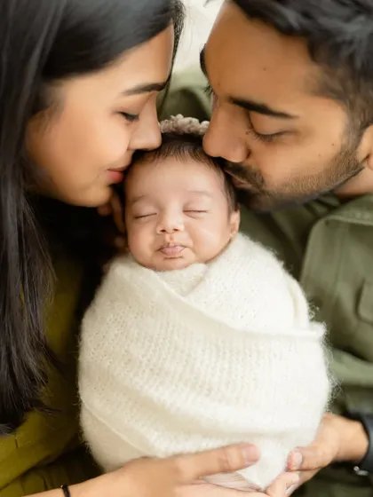 A beautiful family moment, with both parents gently kissing their sleeping newborn's head. The symmetry and emotion make this a truly special portrait.