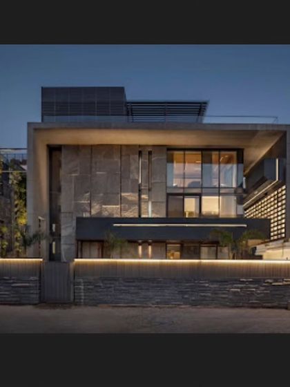 The facade of the 'Green Court Villa' at night. The combination of raw stone, large glass panels, and warm illumination creates a welcoming and sophisticated presence on the street.