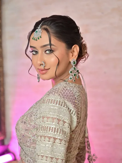 A stunning portrait of a bride with a chic updo and face-framing tendrils. The diamond and emerald jewellery set adds a pop of color to her silver-grey outfit.