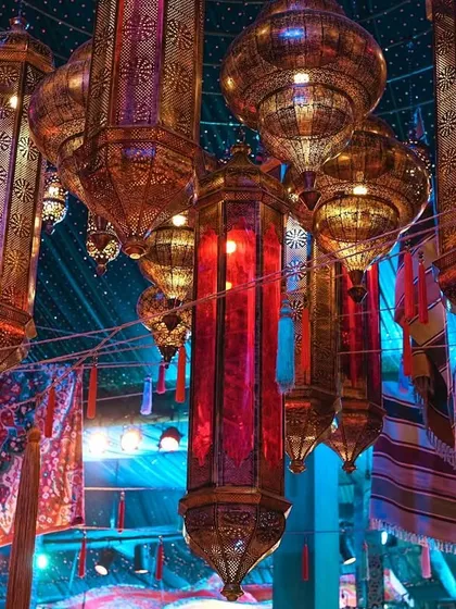 A cluster of ornate Moroccan lanterns hanging from the ceiling. The colorful glass and intricate metalwork cast beautiful patterns, adding to the authenticity and magical ambiance of the Arabian Nights theme.